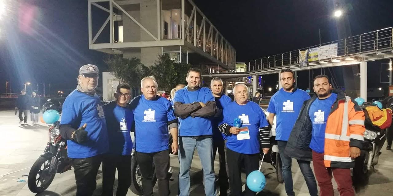 Μέλη με μπλε μπλουζάκια ευαισθητοποίησης για τον αυτισμό, βράδυ, δίπλα σε μοτοσυκλέτες